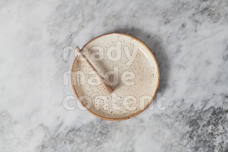 Beige pottery plate with wooden honey dipper in it on grey marble background