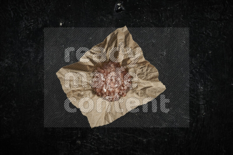 A crumpled piece of paper full of pink himalayan salt on black background