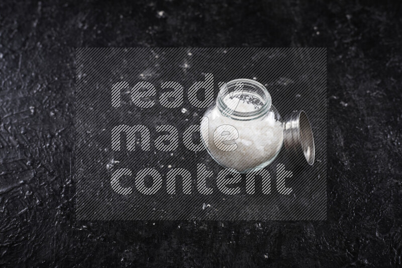 A glass jar full of coarse sea salt crystals on black background