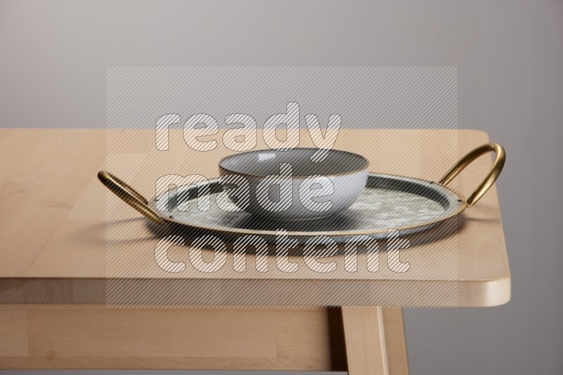 multicolored bowl placed on a rounded stainless steel tray with golden handels on the edge of wooden table