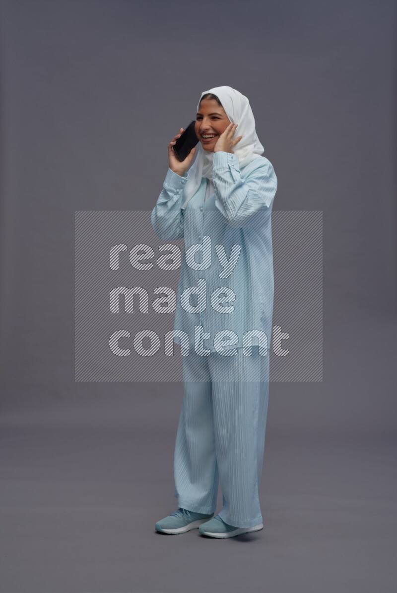 Saudi woman wearing hijab clothes standing talking on phone on gray background