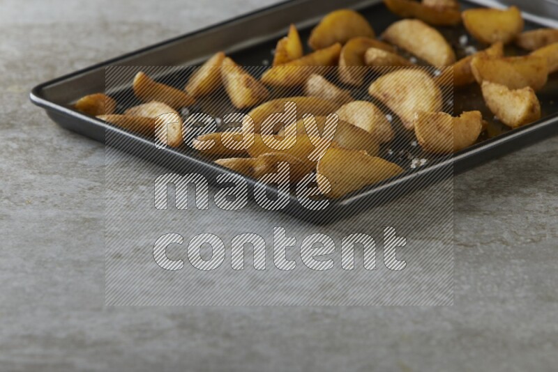 wedges potato in a black stainless steel rectangle tray on grey textured counter top