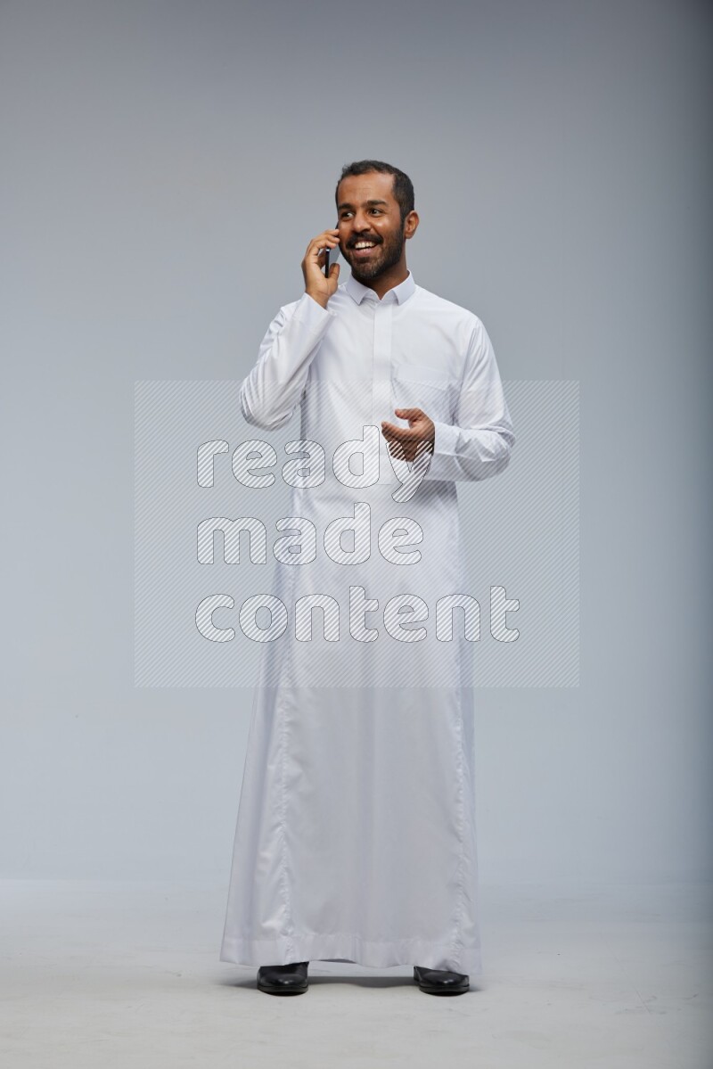 Saudi man wearing Thob standing talking on phone on Gray background