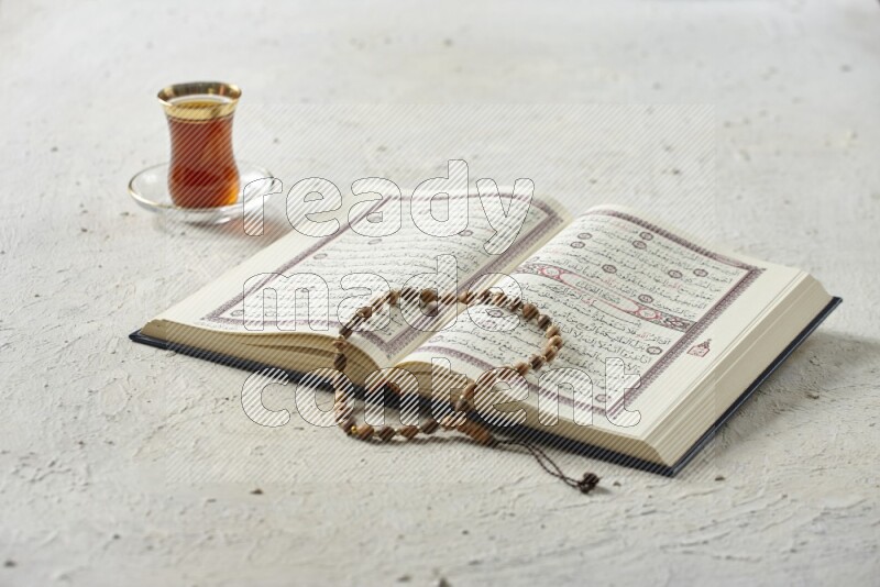 Quran with dates, prayer beads and different drinks all placed on textured white background