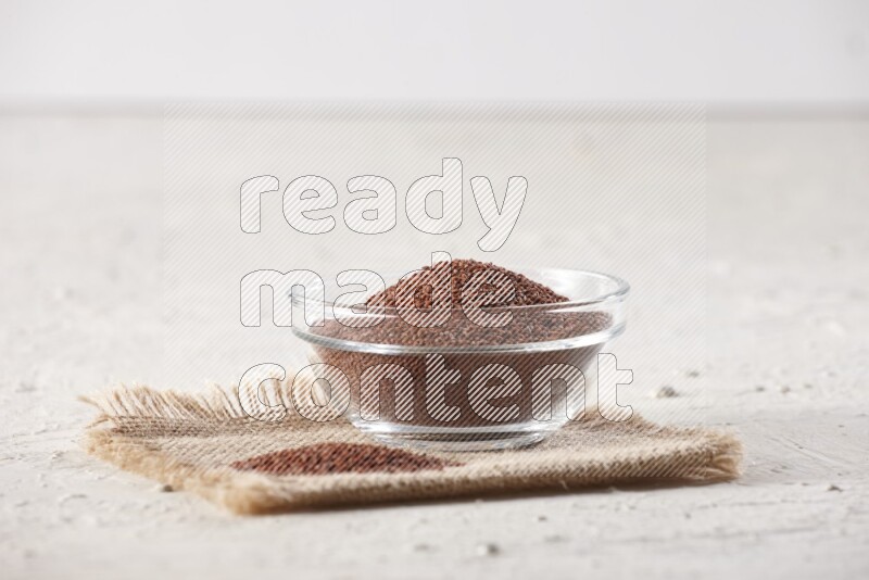 A glass bowl full of garden cress seeds on a burlap fabric on textured white flooring