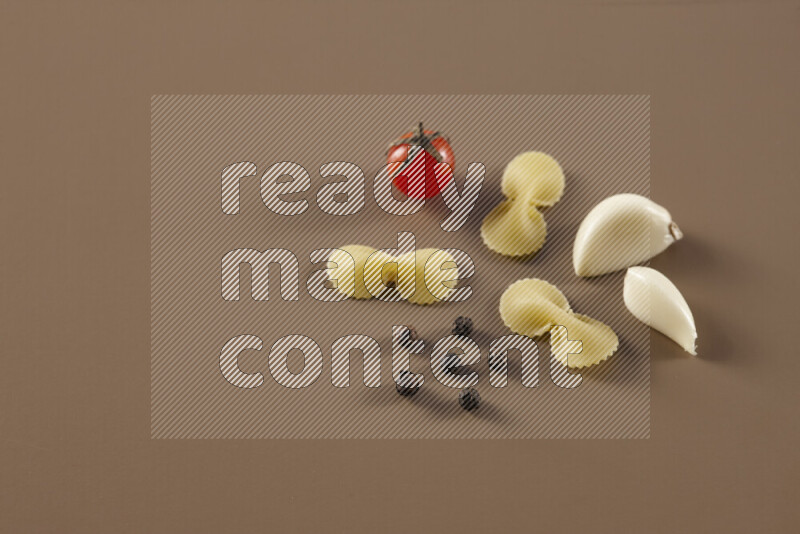 Raw pasta with different ingredients such as cherry tomatoes, garlic, onions, red chilis, black pepper, white pepper, bay laurel leaves, rosemary and cardamom on beige background