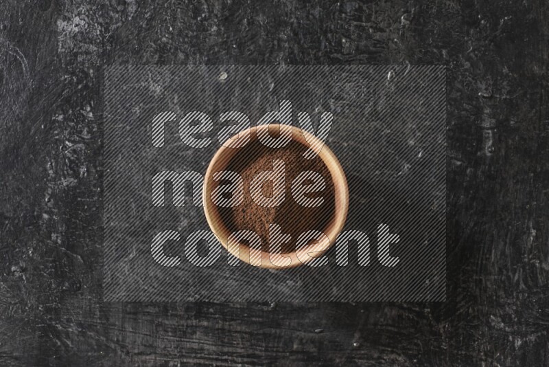 A wooden bowl full of cloves powder on a textured black flooring
