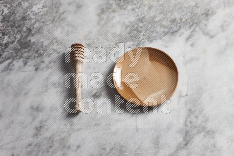 Multicolored pottery plate with wooden honey dipper on the side on grey marble background