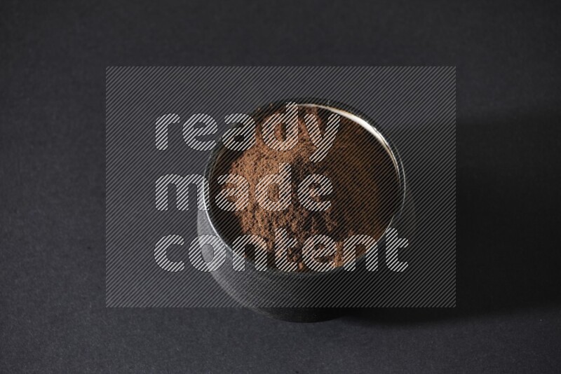 A black pottery bowl full of cloves powder on a black flooring