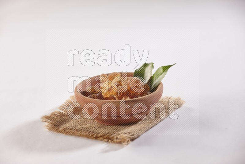A wooden bowl full of gum arabic on a piece of burlap on white flooring