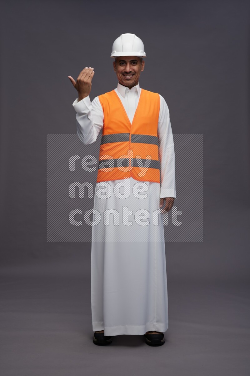 Saudi man wearing thob with engineer vest standing interacting with the camera on gray background