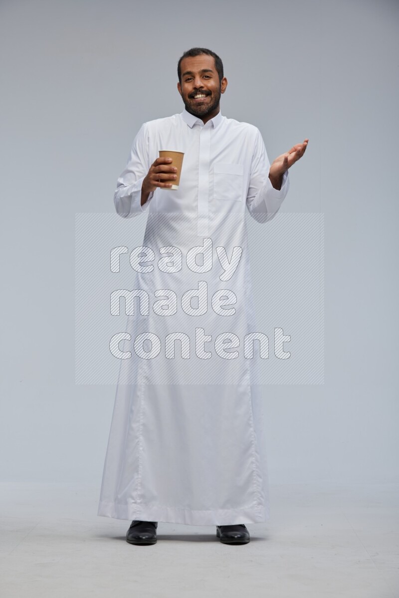 Saudi man wearing thob standing holding paper cup on gray background
