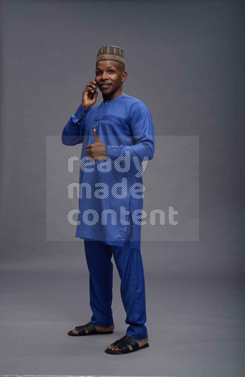 Man wearing Nigerian outfit standing talking on phone on gray background