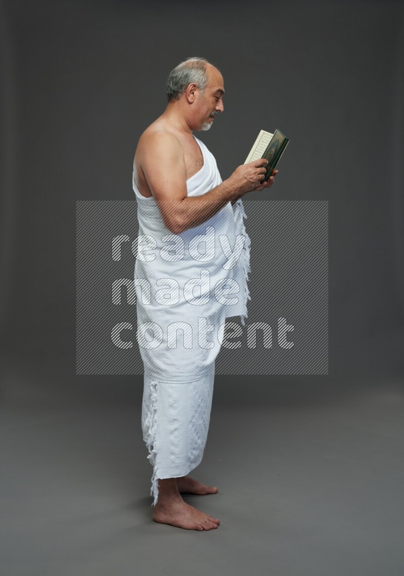 A man wearing Ehram Standing reading quran on gray background