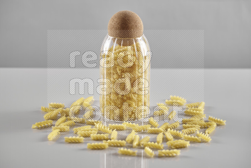 Raw pasta in a glass jar on light grey background