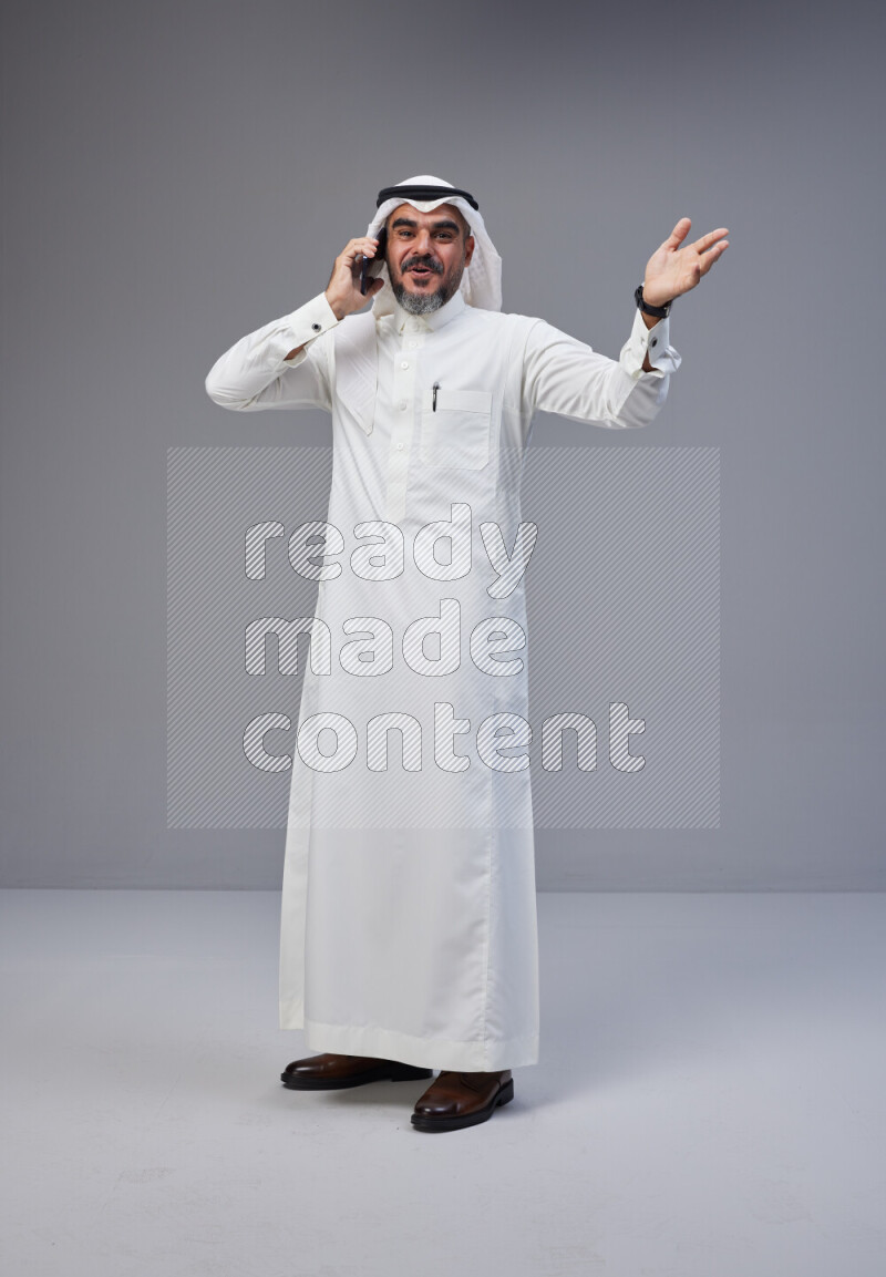 Saudi man Wearing Thob and white Shomag standing talking on phone on Gray background