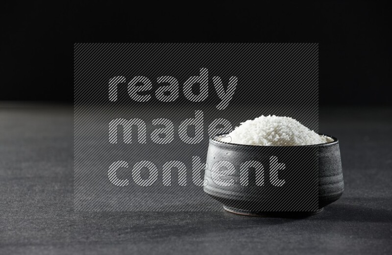 A black pottery bowl full of desiccated coconut on a black background in different angles