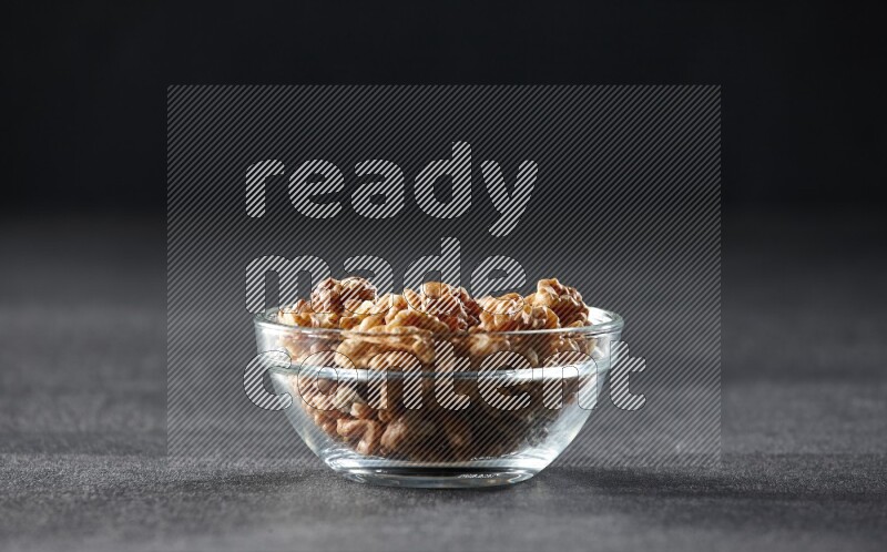 A glass bowl full of peeled walnuts on a black background in different angles