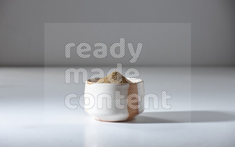 A beige bowl full of cumin powder on a white flooring