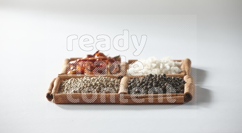 4 مربعات من أعواد القرفة ممتلئة بالفلفل الأحمر والملح والفلفل الأبيض والفلفل الأسود على أرضية بيضاء