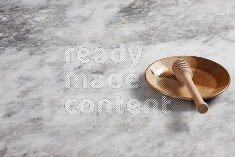 Multicolored pottery plate with wooden honey dipper in it on grey marble background
