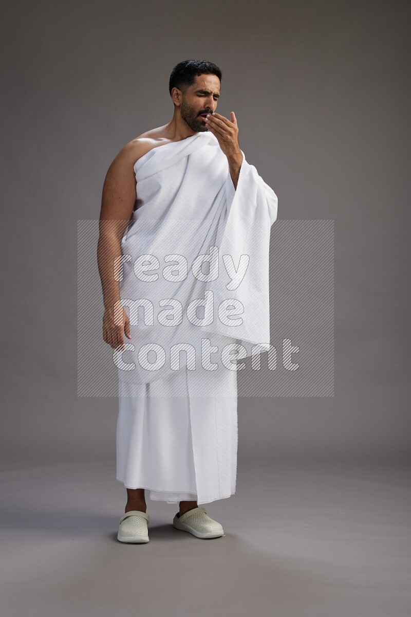 A man wearing Ehram standing showing how to sneeze on gray background