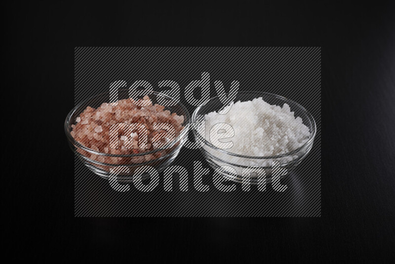 2 glass bowls one is filled with himalayan salt and the other with white salt on black background