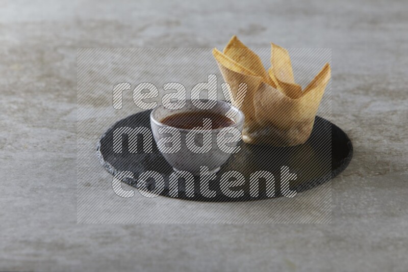 wonton cups with soy sauce ramkin on circle slate on grey textured counter top