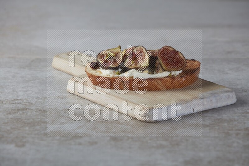 figs halves with cream cheese on toasted sourdough slice on a wooden board on textured grey background