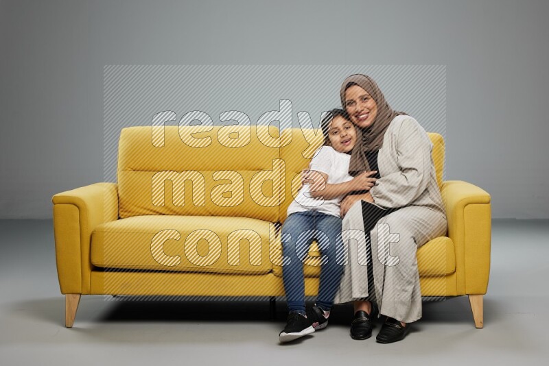 A girl with her mother sitting and interacting with the camera on gray background