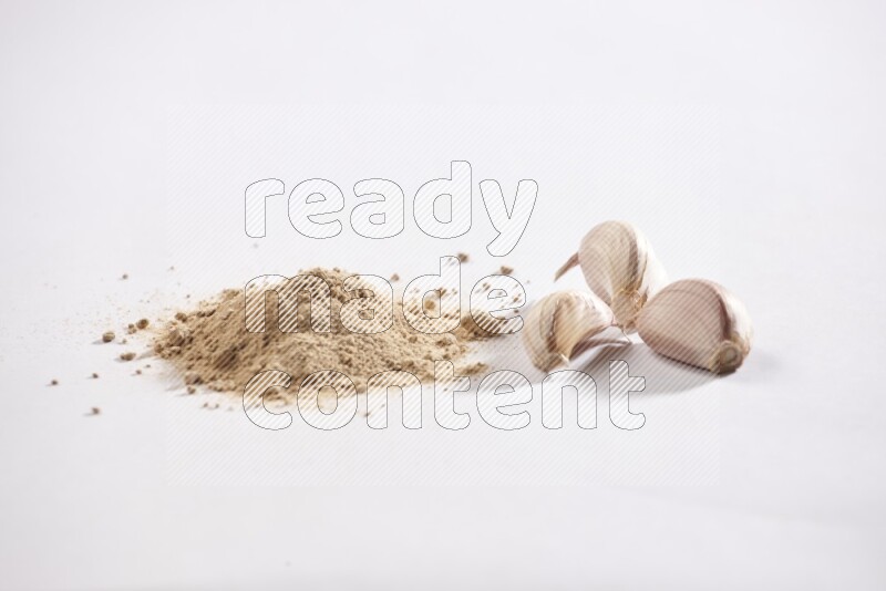 A small pile of garlic powder with some of cloves and a whole garlic bulb on a white flooring