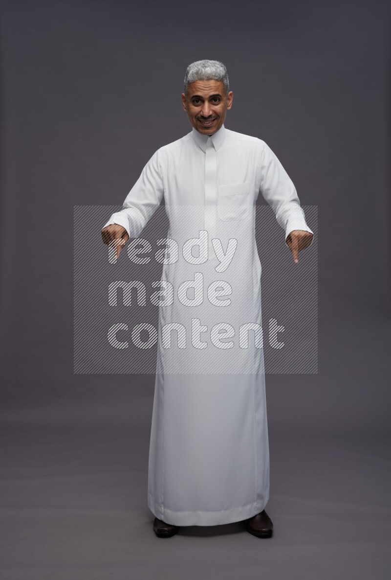 Saudi man wearing thob standing interacting with the camera on gray background