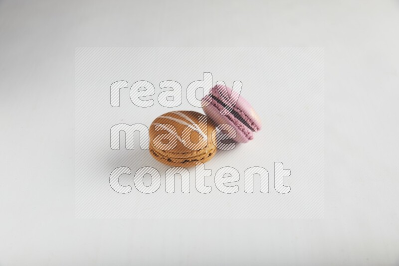 45º Shot of of two assorted Brown Irish Cream, and Purple Strawberry macarons on white background