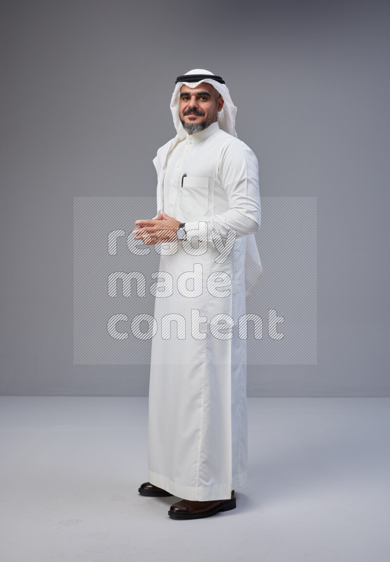Saudi man Wearing Thob and white Shomag standing interacting with the camera on Gray background