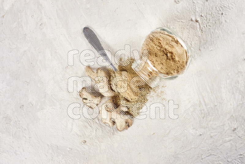 A glass jar full of ground ginger powder flipped with some spilling powder on white background