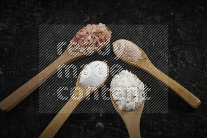 4 wooden spoons filled with fine and coarse salt on black background