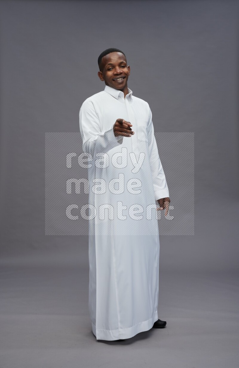 Saudi man wearing thob standing interacting with the camera on gray background