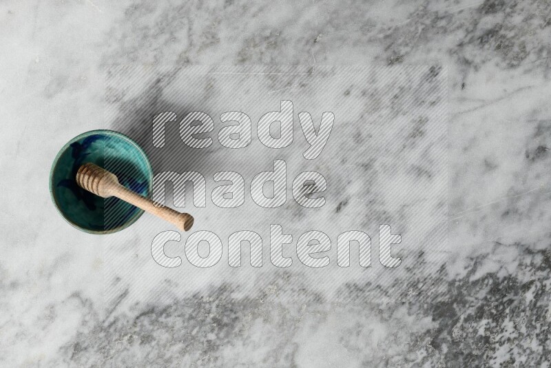 وعاء فخاري مزخرف مع ملعقة عسل خشبية بداخله على خلفية من الرخام الرمادي