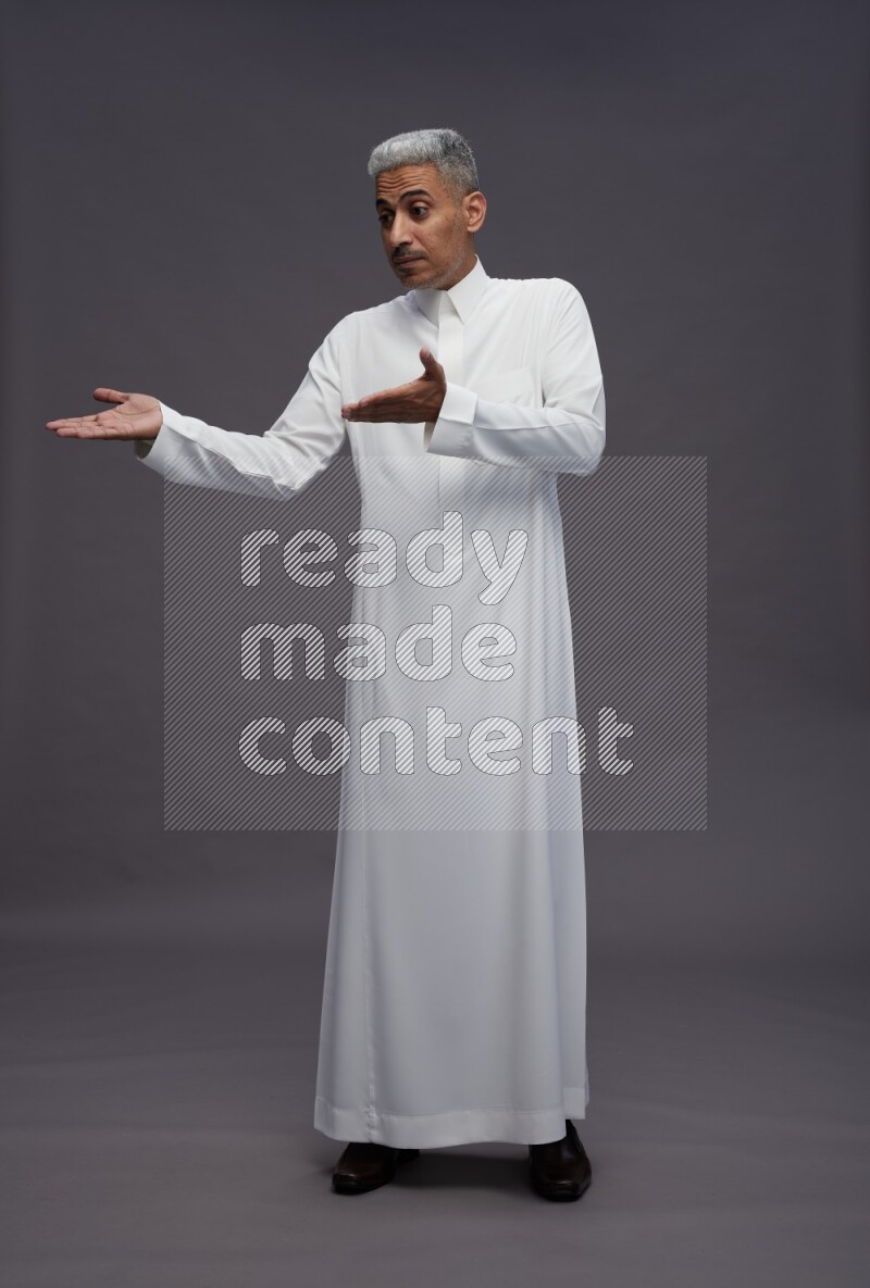 Saudi man wearing thob standing interacting with the camera on gray background