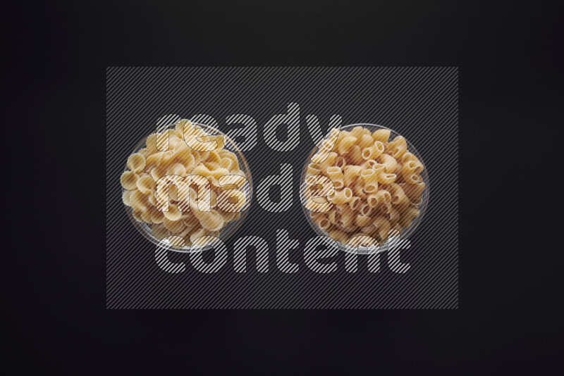Different pasta types in glass bowls on black background