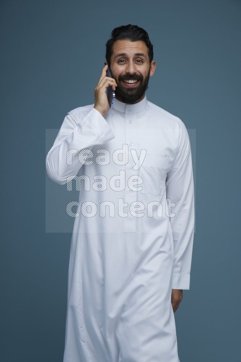 A man having a call on a blue background wearing Saudi Thob
