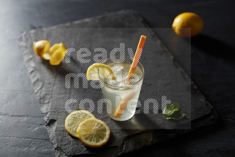 A glass of lemon juice with a straw on black background