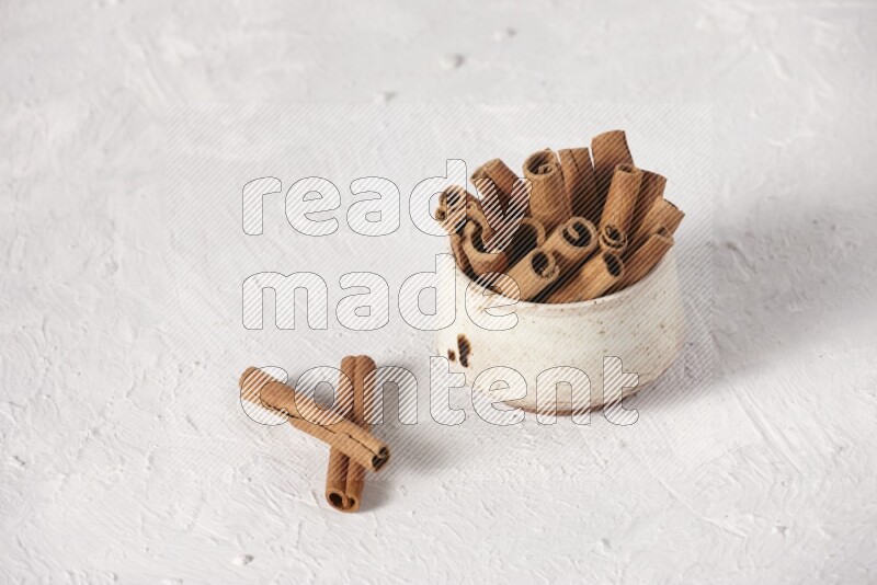 Cinnamon sticks in a beige bowl on a white background
