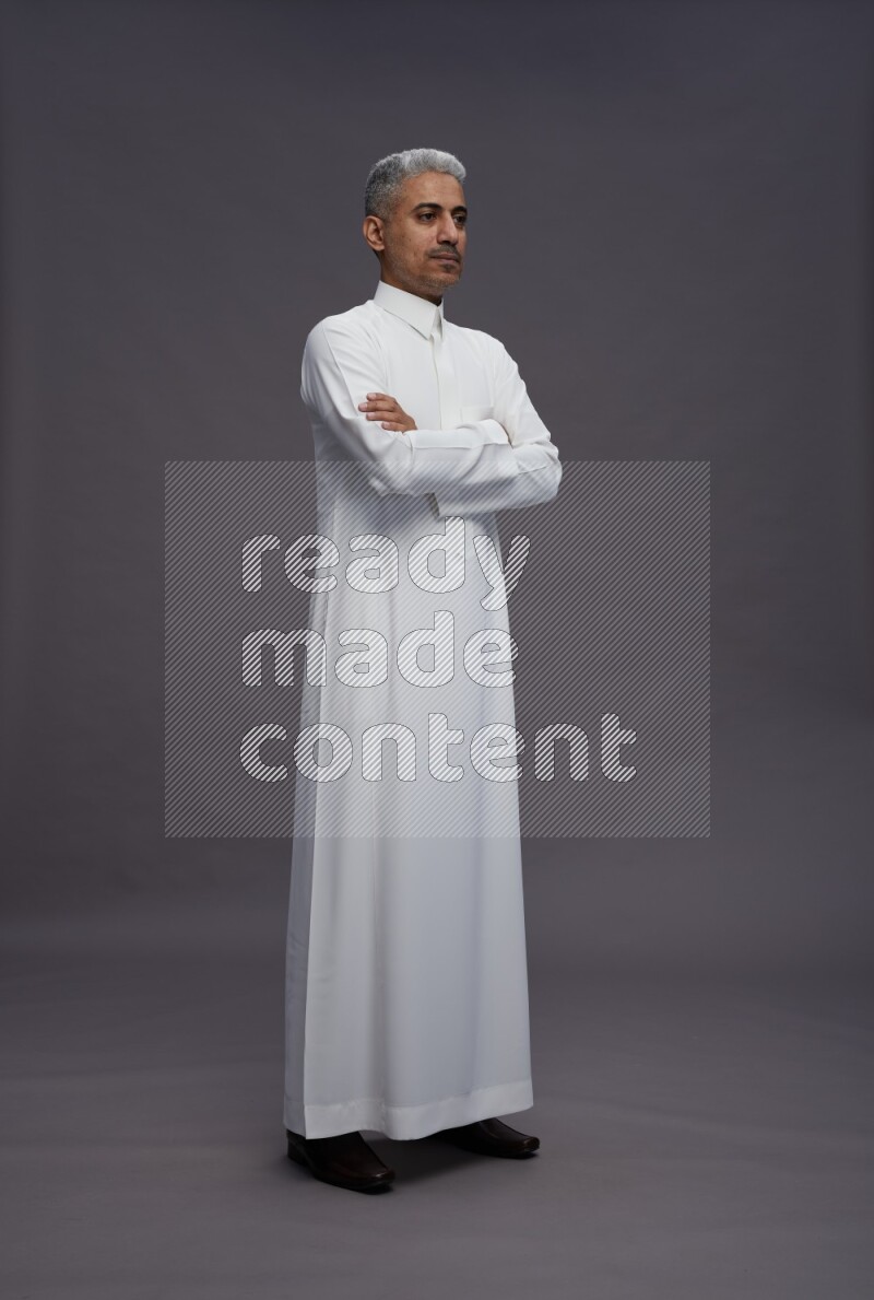 Saudi man wearing thob standing with crossed arms on gray background