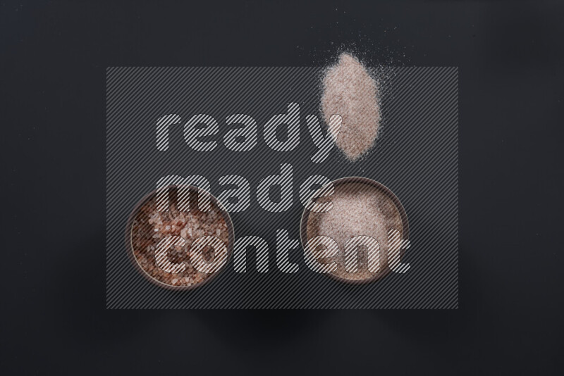 Pottery bowl full of fine himalayan salt and coarse himalayan salt on black background