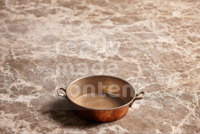 A small copper pan on beige marble background