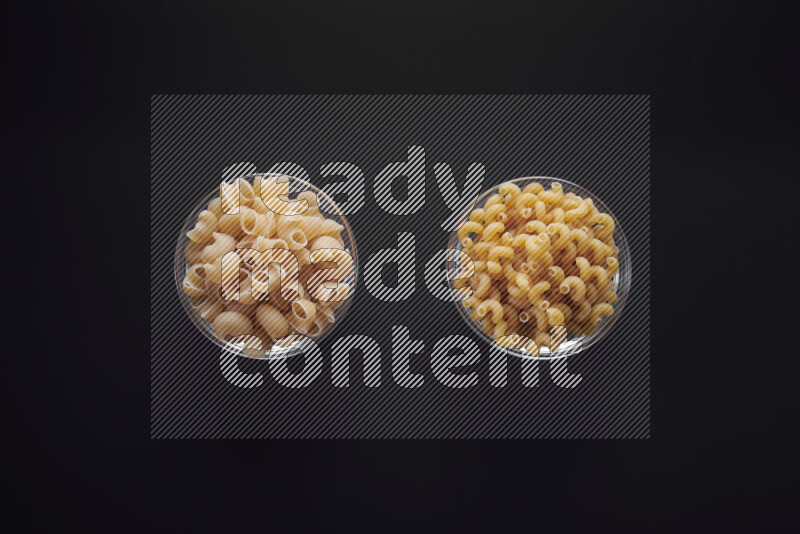 Different pasta types in glass bowls on black background