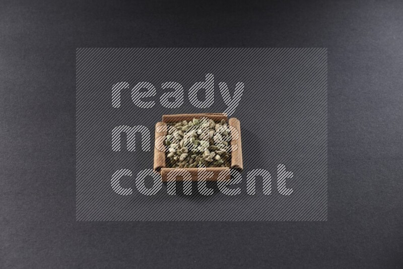 أربعة من أعواد القرفة مكونة شكل مربع بداخلها حبوب الهيل علي خلفية سوداء