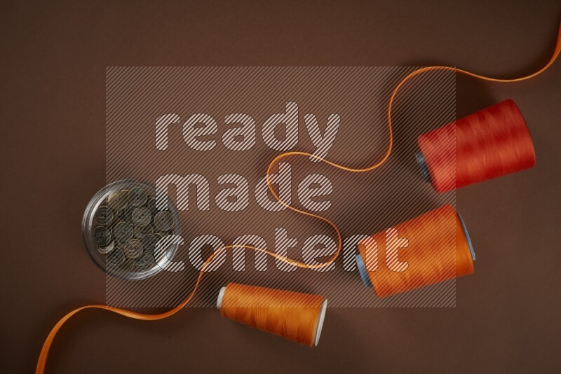 An orange collection of sewing and tailoring tools arranged on a brown background