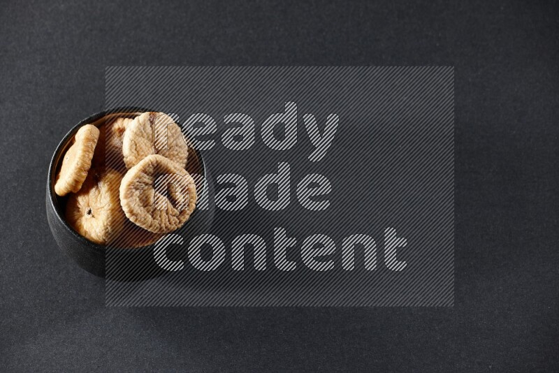 A black pottery bowl full of dried figs on a black background in different angles